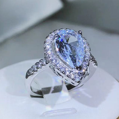 Elegant diamond ring with a pear-shaped center stone on a white stand.